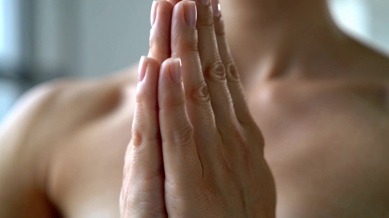 Donna a spalle scoperte che unisce le mani al petto in studio, cercando calma e mostrando le unghie