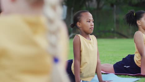 mixed race schoolgirls lying on mats streching during yoga class outdoors