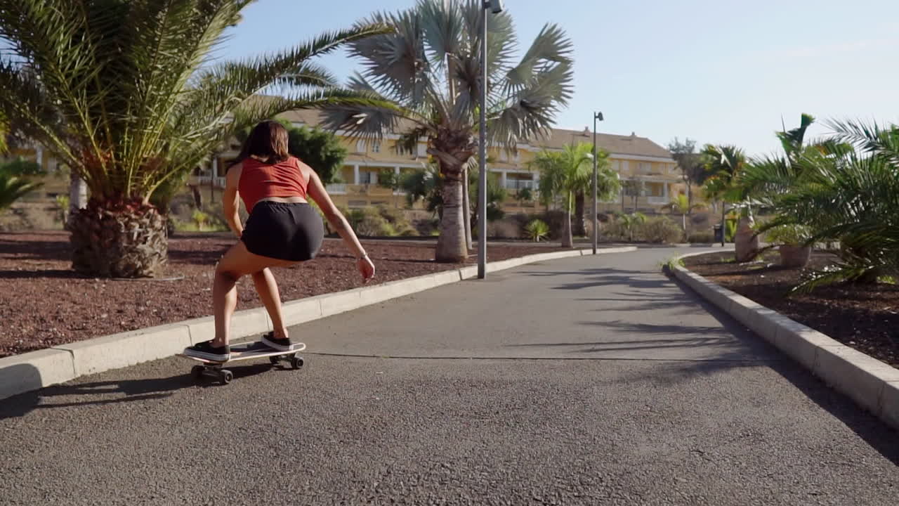 Slow motion portrays a mesmerizing scene: a young girl skillfully riding her longboard by the beach and palm trees
