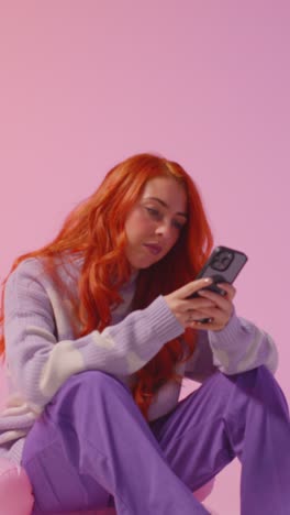 Vertical-Video-Studio-Shot-Of-Young-Gen-Z-Woman-Gaming-Streaming-Or-Using-Social-Media-On-Mobile-Phone-Against-Pink-Background