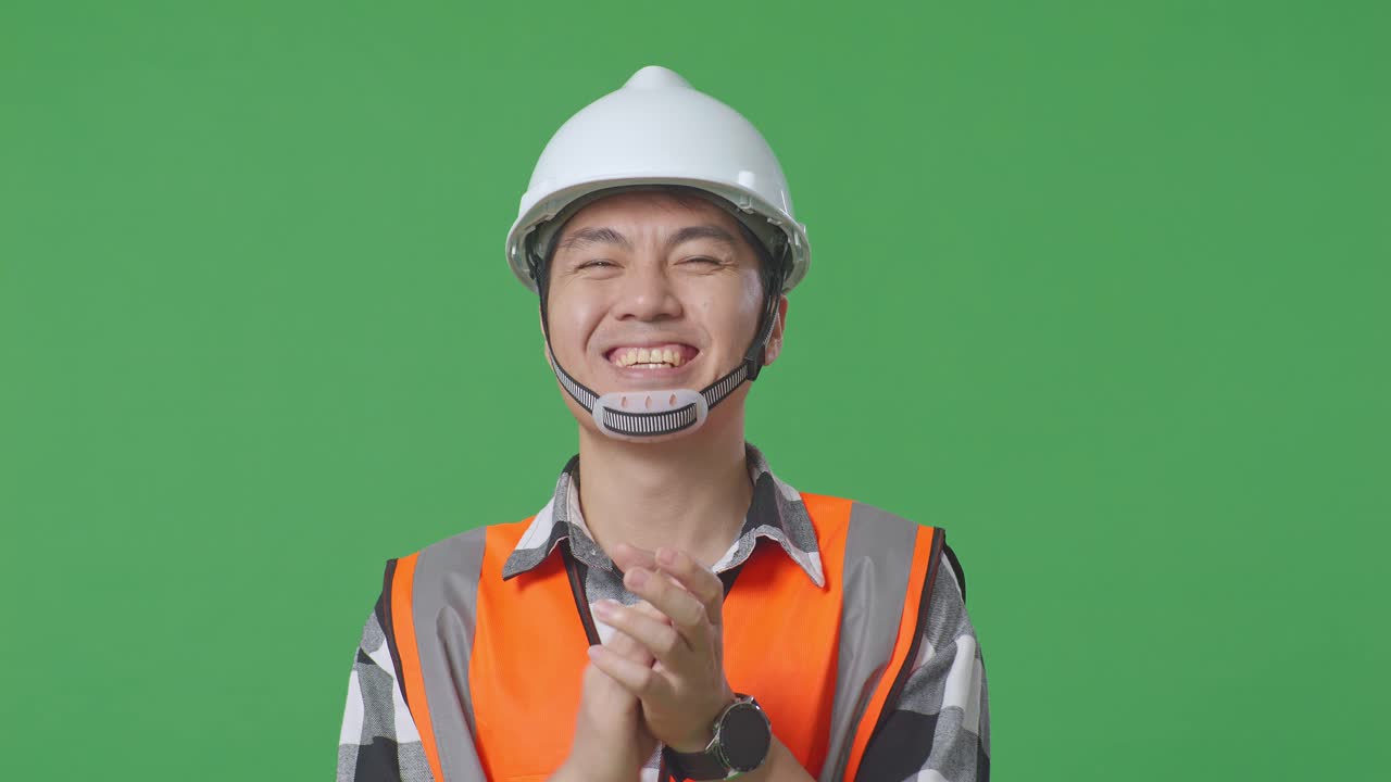 Close Up Of Asian Male Engineer With Safety Helmet Smiling And Clapping His Hands While Standing In The Green Screen Background Studio
