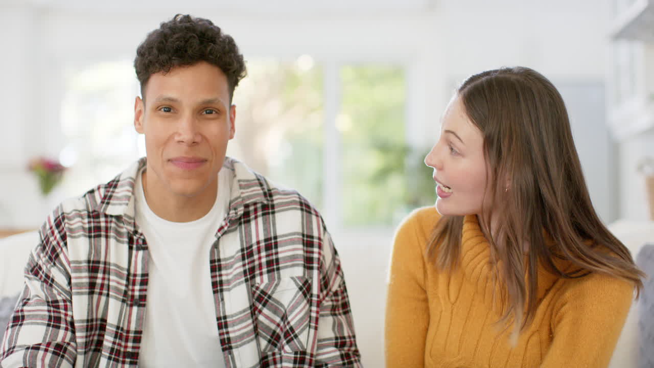Happy diverse couple sitting on sofa having video call at home, in slow motion