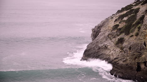 dramatic ocean waves crashing against a rocky cliff coast