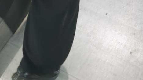 lower angle view of person in black pants and dark sneakers stepping off escalator, showing detailed motion and transition from mechanical steps to solid ground in indoor environment