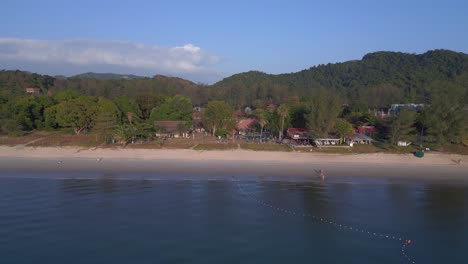 Tourists-enjoying-walking-on-the-beach-at-sunset-with-lush-green-tropical-forest-in-the-background