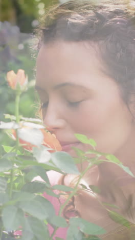 animation of glowing lights over happy biracial woman smelling flowers in garden