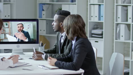 tracking shot of diverse business team listening to mid aged entrepreneur and writing down notes at web conferencing in the office