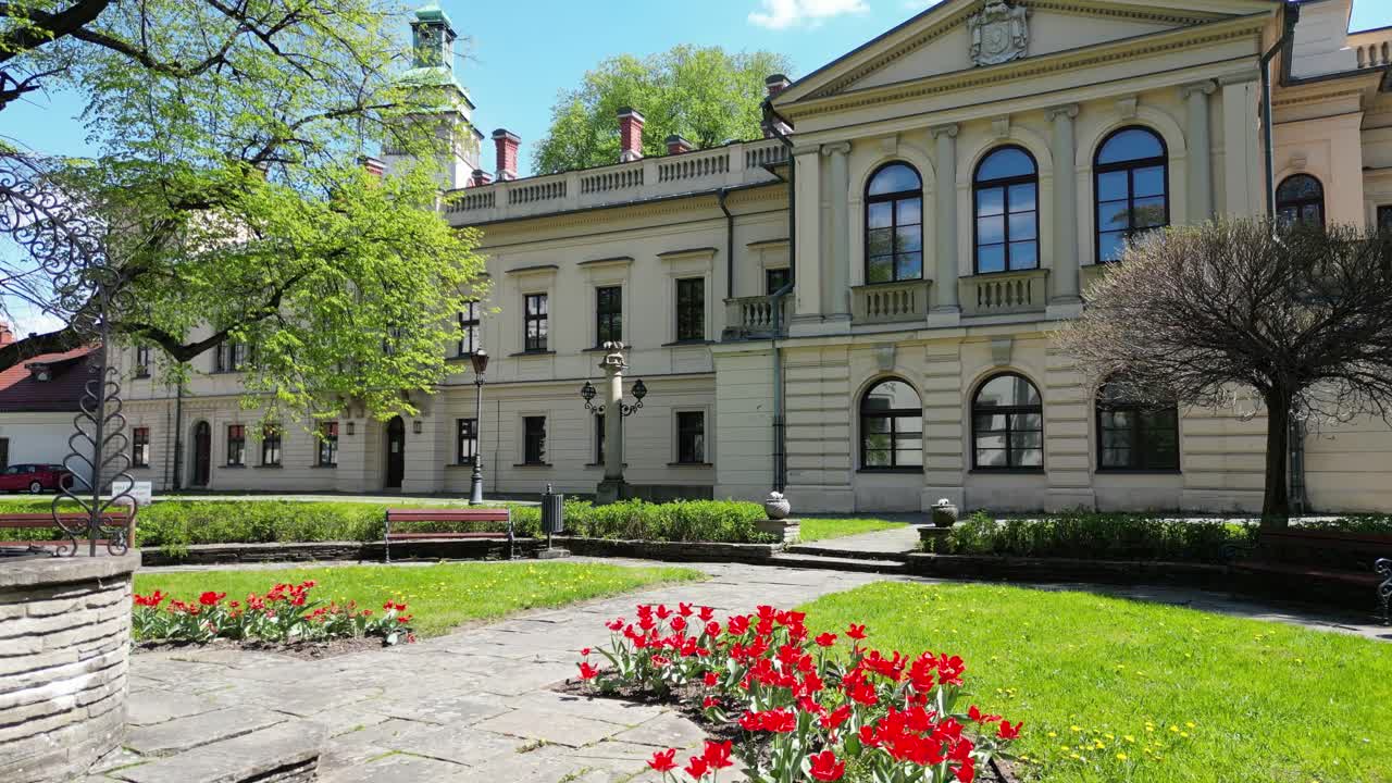 A well in front of the old castle in Zywiec on sunny day - palace facade aerial 4k