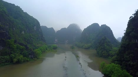 cinematic drone footage of majestic limestone peaks in misty and foggy weather. ricefields in wild jungle in the spring with boat tour canal in tam coc, ninh binh, vietnam