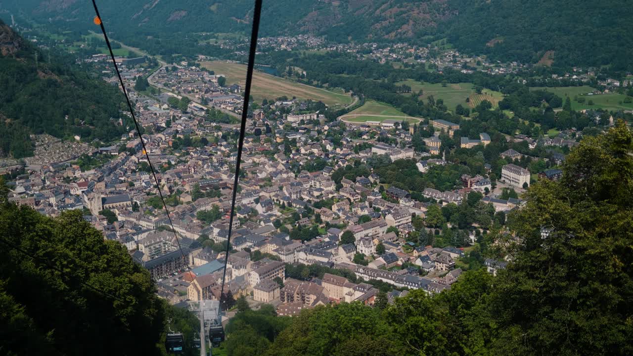 Cable car view descending over picturesque town in lush valley surrounded by mountains and greenery