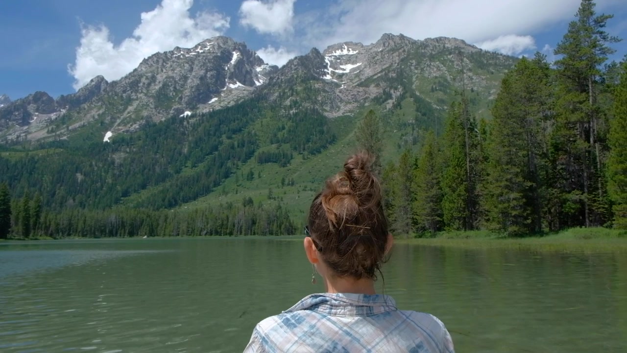 Caucasian woman center framed taking photo with phone of Grand Tetons from a kayak