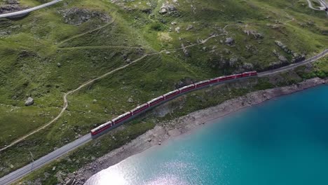 Aerial-clip-showing-a-train-moving-along-the-green-hills-adjutant-to-a-lake-with-blue-water