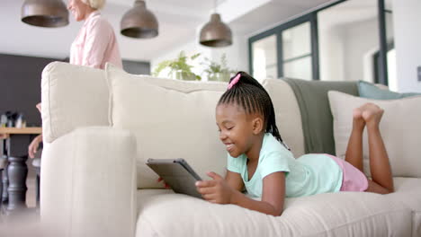 african american girl lies on a sofa using a tablet, her smile suggesting enjoyment