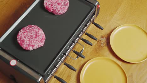 utensil putting handmade raw burgers on plancha grill. static medium shot