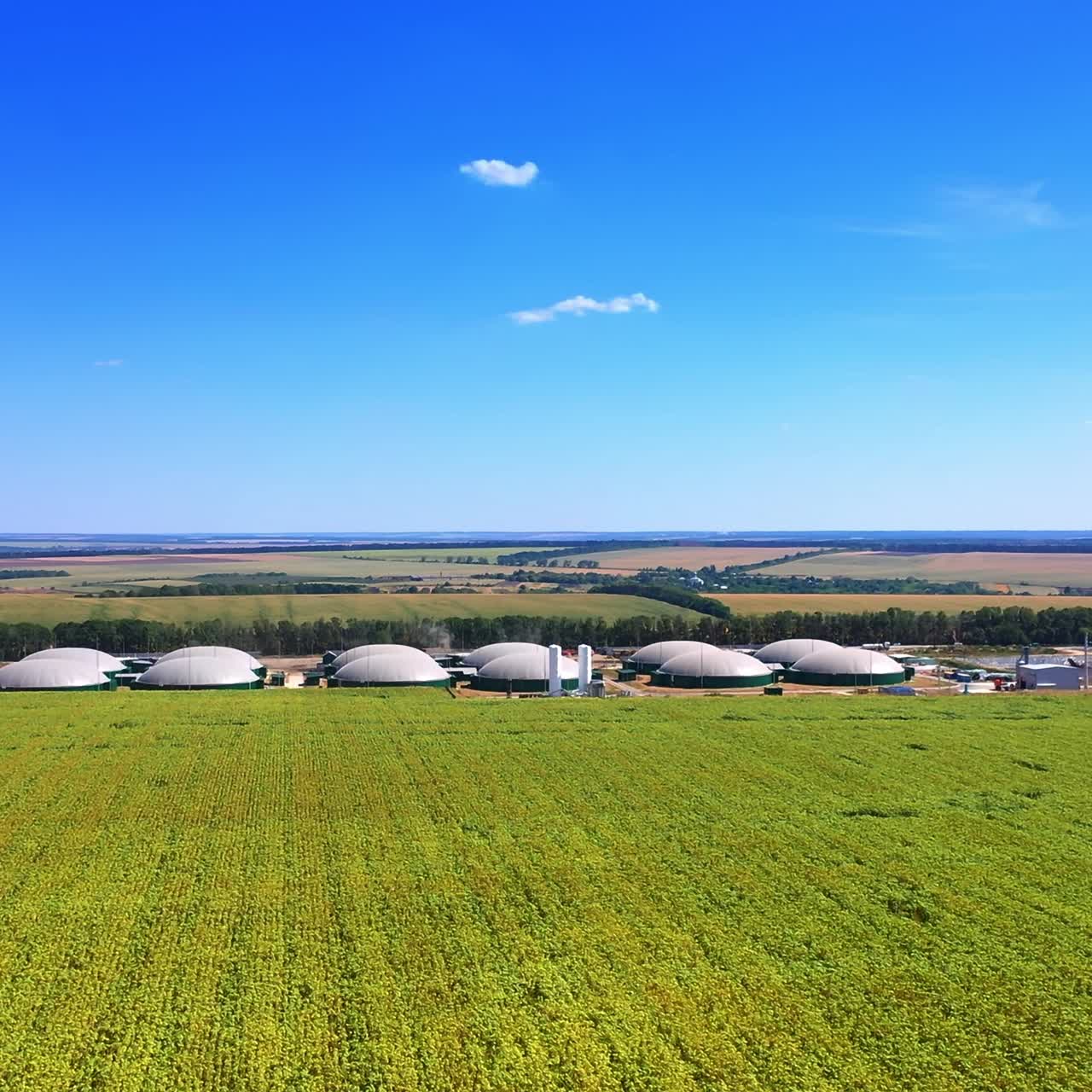 Vast farmlands surrounding the modern biogas factory. Drone approaching the cupolas of bio fuel plant. Top view
