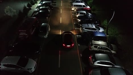 car driving down avenue lined with nearly full parking spots as pedestrians cross the street - drone view