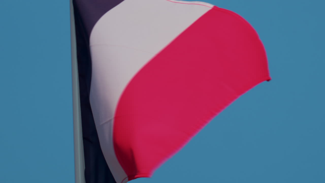 A close up of the French national flag waving gracefully in the wind under a clear blue sky