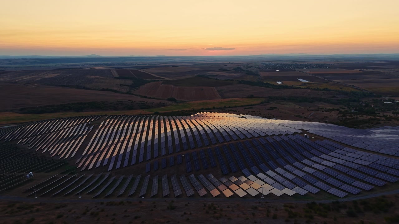 Solpaneler dækker et stort område på et landligt sted ved solnedgang med varme farver på himlen