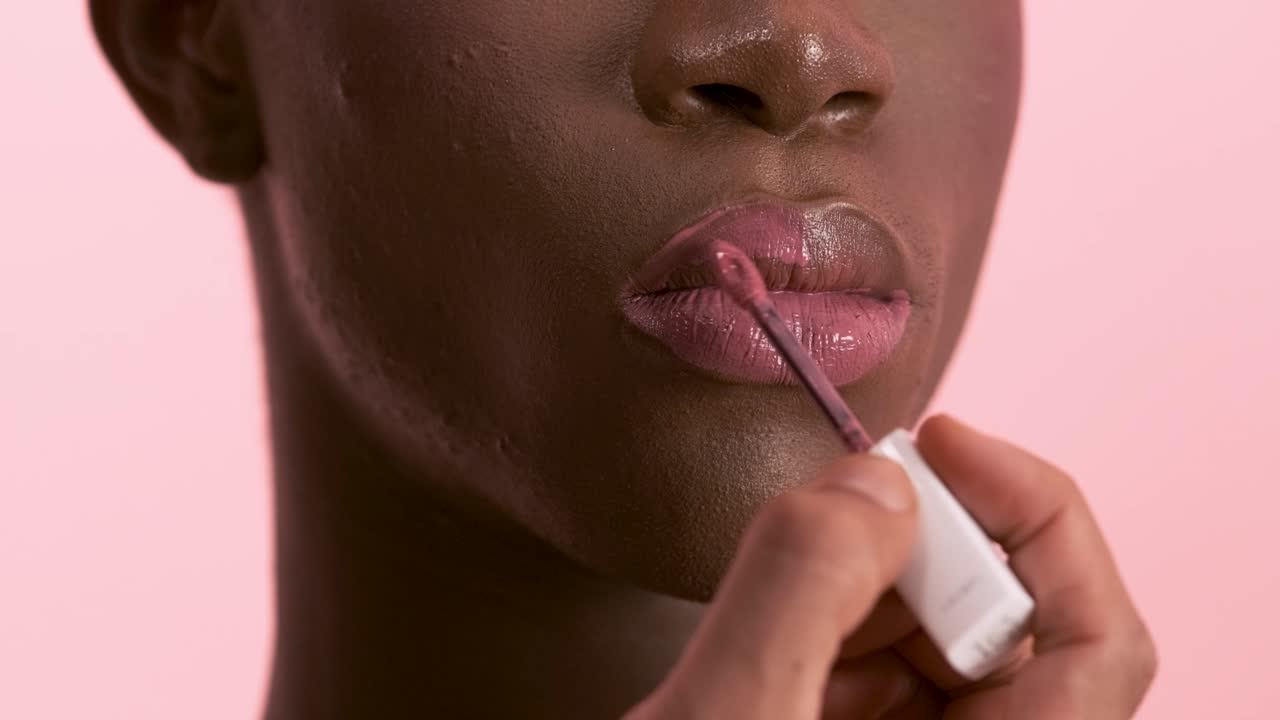 Visagiste applying lip gloss while doing makeup on black transgender model