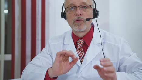 portrait of senior doctor in glasses and headset. professional male physician in white medical uniform speaking looking at camera.