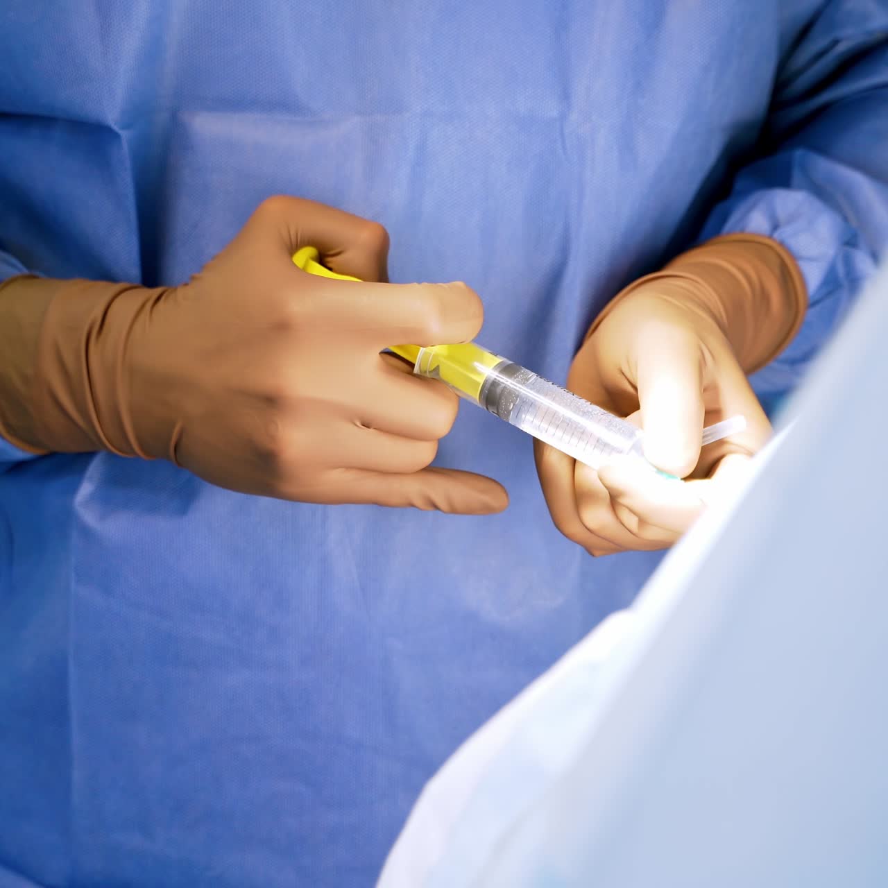 Doctor's hands in gloves with syringe. Medical specialist in blue uniform doing an injection to a patient. Close-up.