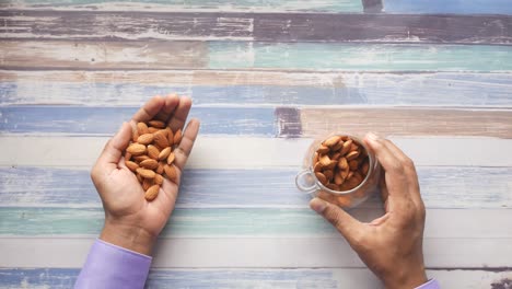 almonds in hands and glass cup on wooden table