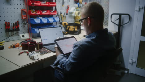 employee checking real-time stocks and exchange market charts using digital tablet and laptop. man making investments during working hours in workshop, combining job with online trading. vertical shot