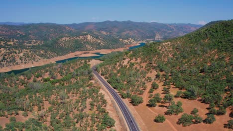 aerial drone shot of a car driving on the scenic road along the lake on a sunny day