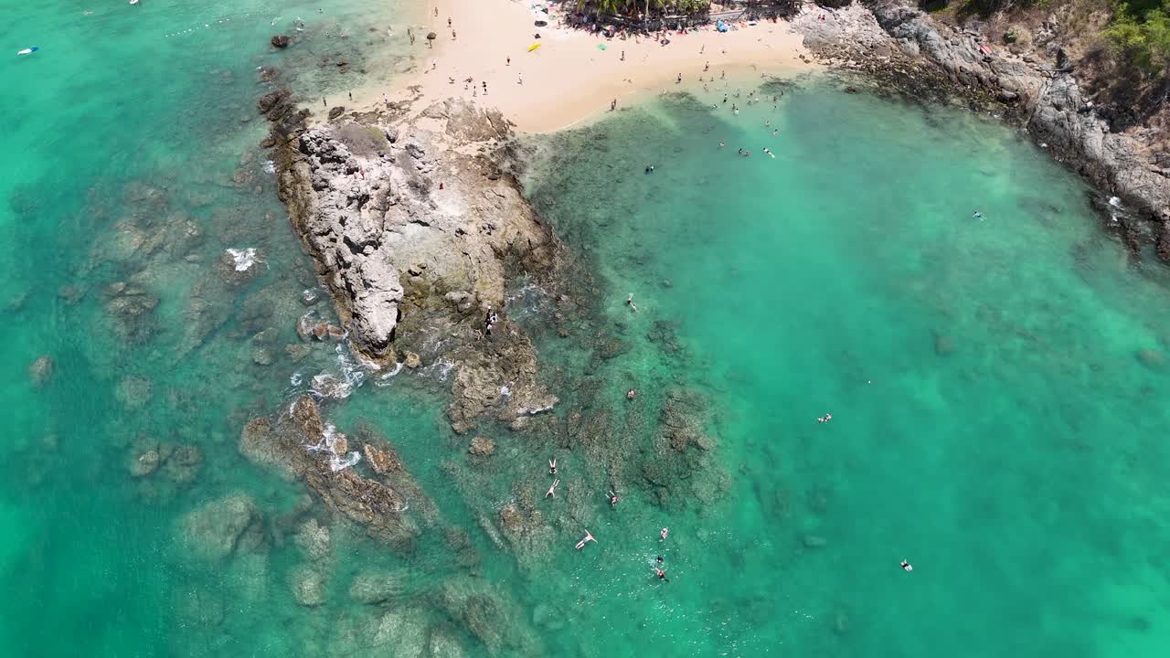 Drone çekimi, Tayland'ın Phuket adasında turkuaz suları ve kayalık kıyı şeridini sergileyen el değmemiş bir plajın çarpıcı havadan görünümünü yakalıyor.