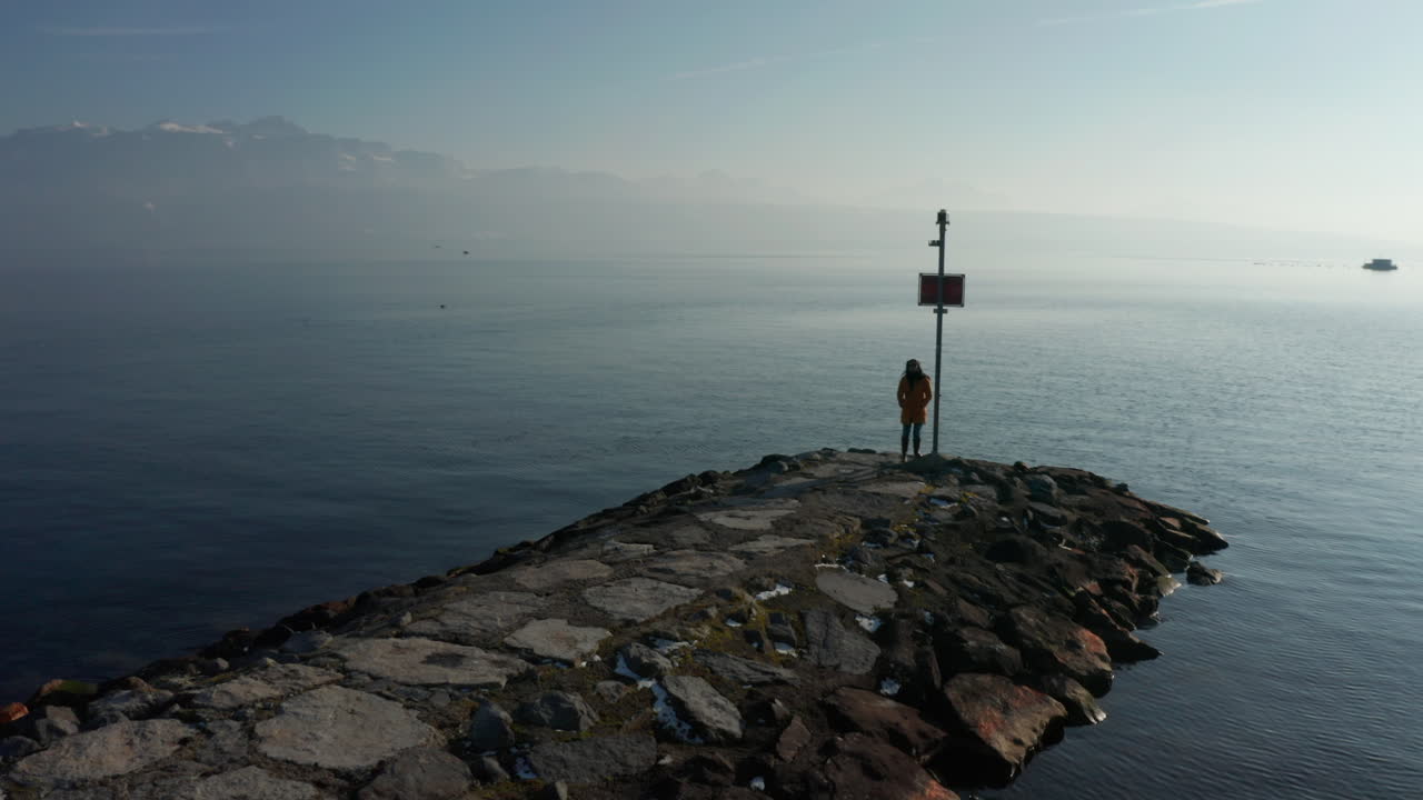 Aerial dolly of woman standing on stone quay at lake Geneva, Switzerland