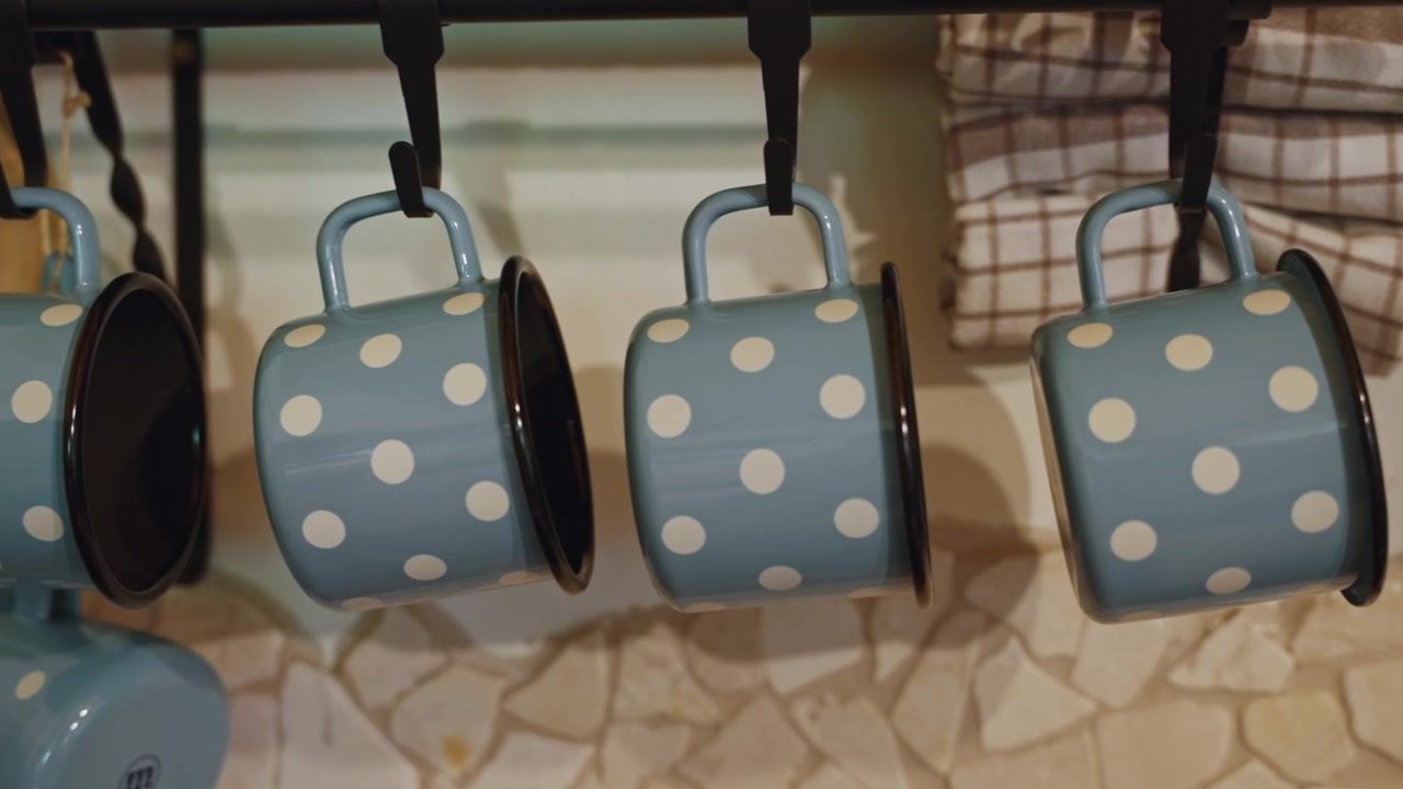 Charming pastel blue polka dot mugs hang neatly in a cozy rustic kitchen. Soft lighting highlights vintage details in this close-up shot.