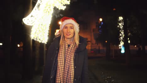 a beautiful woman in a santa claus hat walks at night on christmas