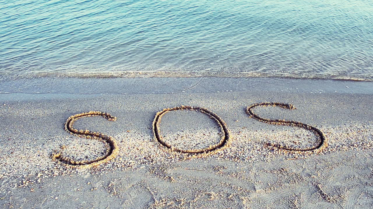 Kum üzerine yazılmış SOS yazısı. Sahilde çekim