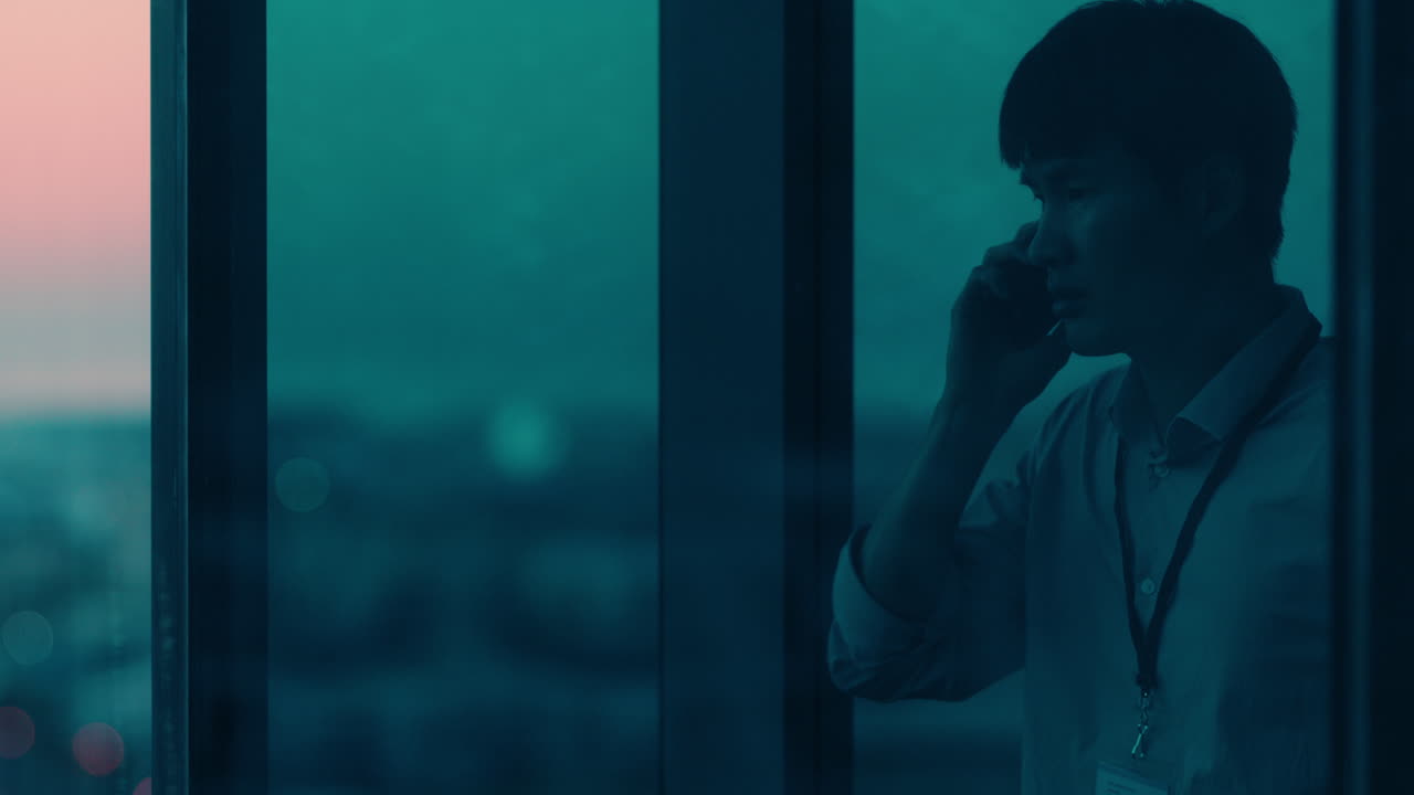 스마트폰을 사용하는 아시아 사업가 고객과 대화 기업 임원 협상 거래 전화 통화 사무실에서 늦게 일해 일몰 때 창문을 바라보고