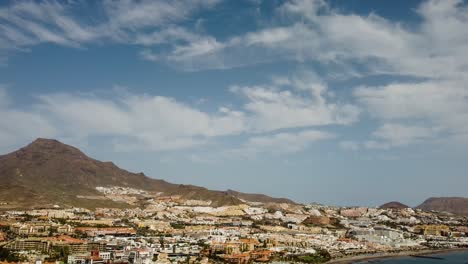 Hermosa-Playa-Con-Montañas-En-El-Fondo-Y-Edificios-En-El-Lado-Del-Mar-Azul-Disparo-De-Drones