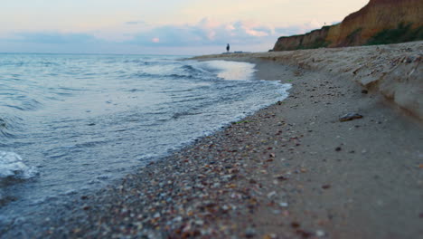 Olas-Del-Mar-Agua-Salpicando-La-Playa-De-Arena-Al-Amanecer.-Mujer-Solitaria-Caminando-Por-La-Playa