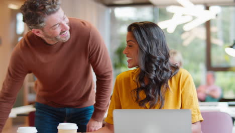 mature male businessman brings takeaway coffee for female colleague as they have meeting with laptop