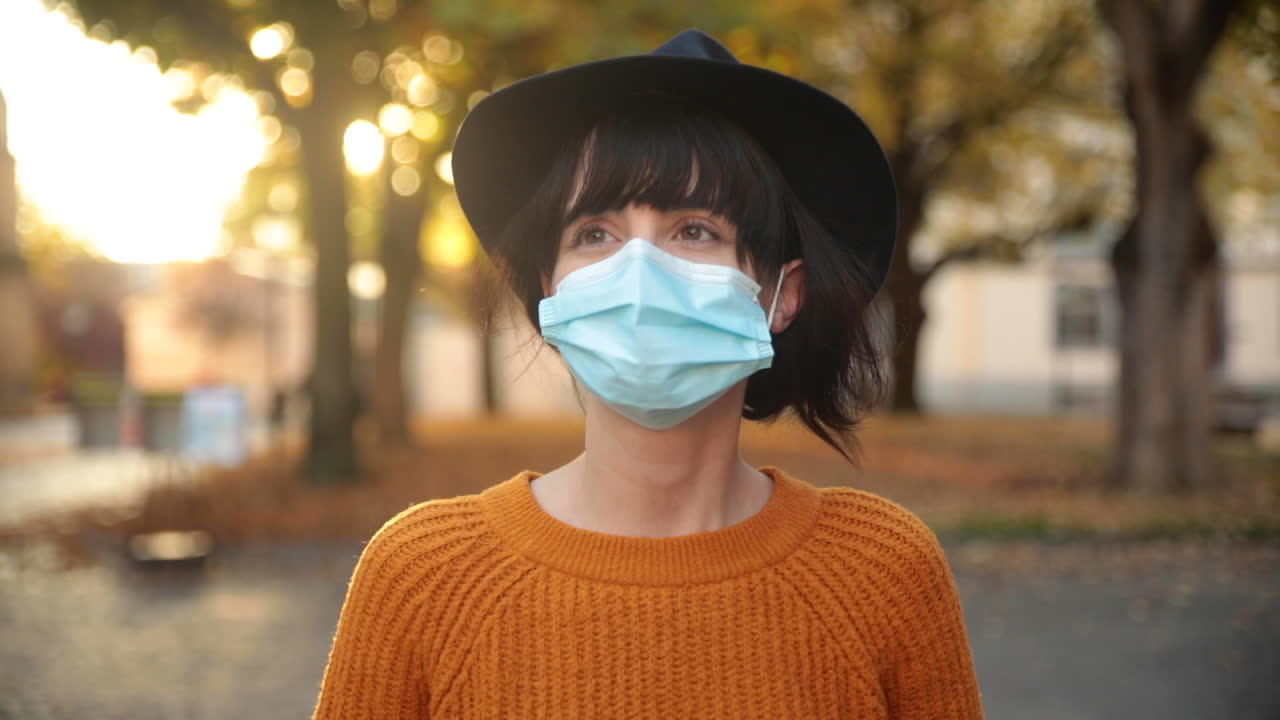 Young brunette woman walking under trees in autumn, wearing a mask during corona in slow motion
