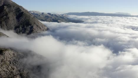 Mountain-range-peaks-rising-above-lows-clouds,-high-aerial-view