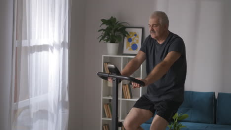 Entrenamiento-En-Casa-En-Bicicleta-Estacionaria,-Un-Hombre-De-Mediana-Edad-Está-Girando-Pedales-En-La-Sala-De-Estar,-Un-Estilo-De-Vida-Saludable-Y-Mantenerse-En-Forma