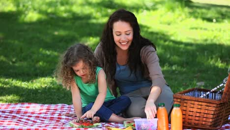 Mother-and-little-daughter-enjoying-strawberries-sitting-on-a-tablecloth