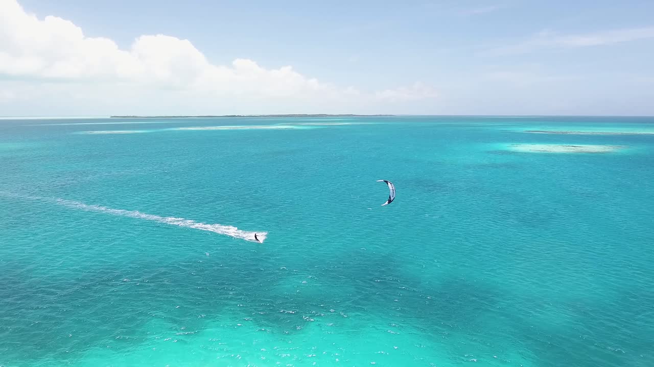 disparo de un dron siguiendo a un hombre haciendo kitesurf en aguas planas del mar caribe, los roques