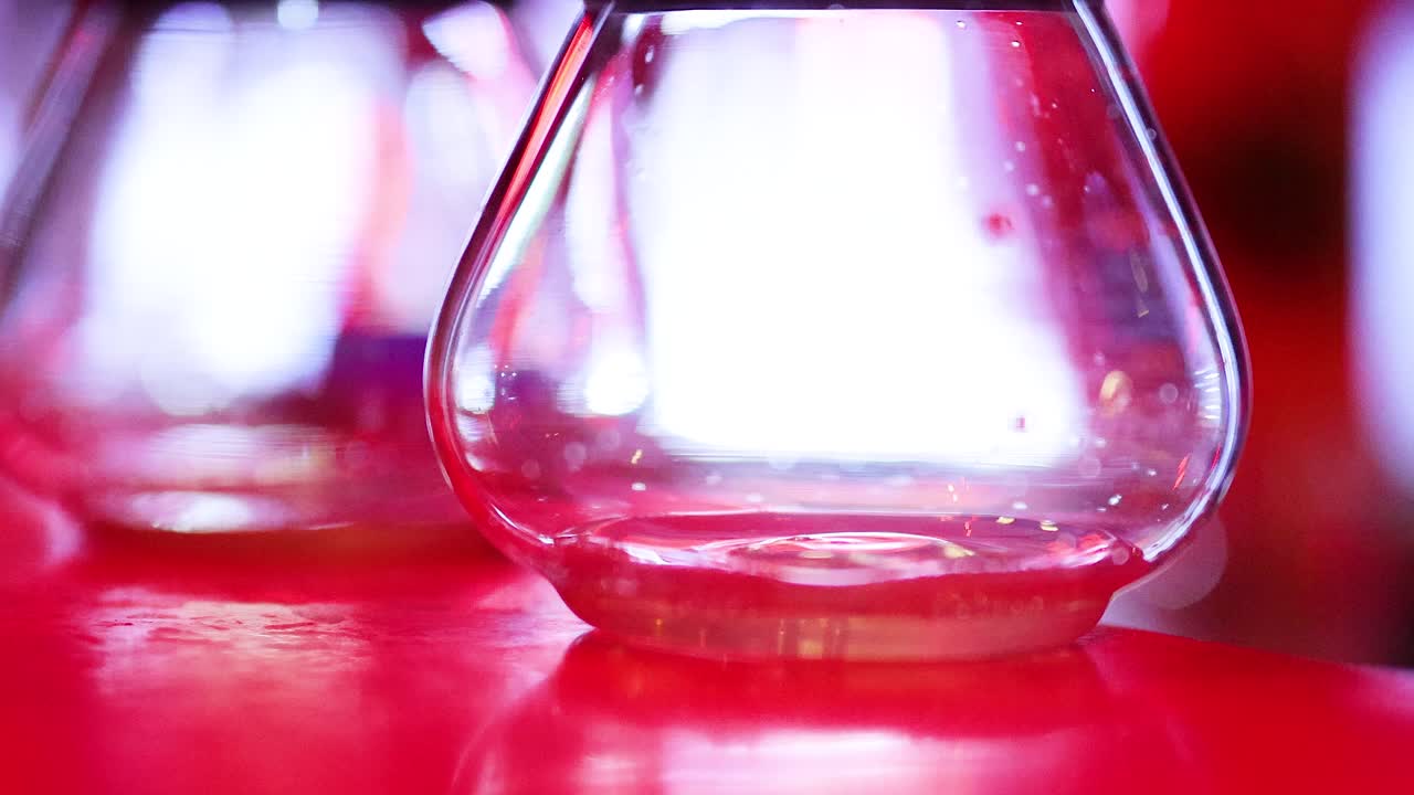 Close-up of liquid drop entering empty glass, vibrant lighting, shallow focus, slow-motion effect
