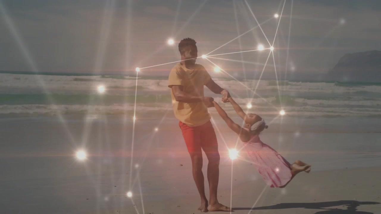 Padre che gioca tenendo per mano e facendo dondolare la figlia in spiaggia, con maglietta gialla e vestito rosa, e un effetto luminoso in sovrapposizione.