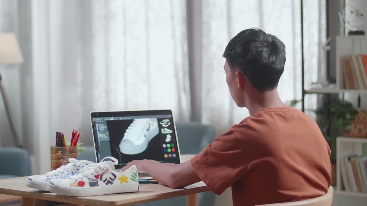 아시안 소년 신발 디자이너는 집에서 노트북에서 작업하는 동안 신발의 3d 모델을 회전합니다. 신발 생산 절차 개념. 사이버 게임 의류 및 신발 라인