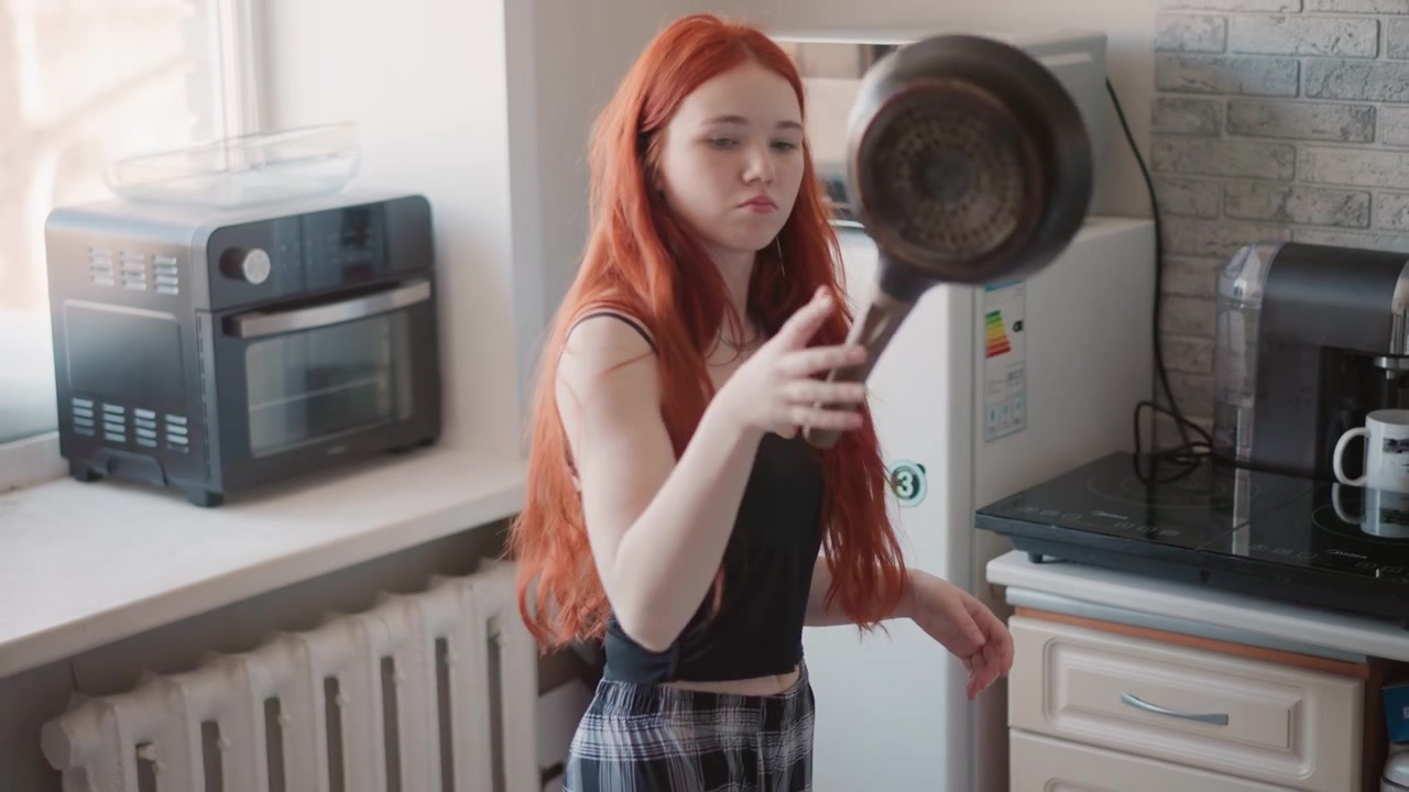 Azione in cucina luminosa, donna caucasica che capovolge una padella sui fornelli, che prepara la colazione con macchina del caffè e uova sul bancone, gonna casual a fantasia, movimento vivace e praticità domestica.