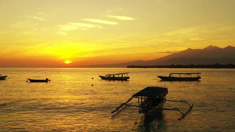 silhouette of traditional balinese fishing boats floating on calm sea surface reflecting beautiful yellow sky sunlight at sunset