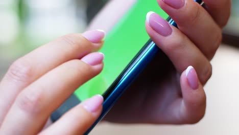 una mujer está sentada en un café con un teléfono inteligente en las manos con una maqueta de pantalla verde. la chica utiliza activamente el teléfono para sus propios propósitos. contenido, videos, blogs.