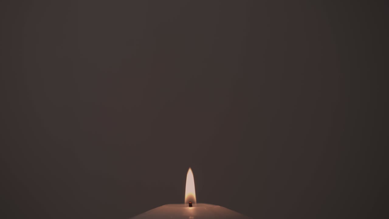 imágenes en primer plano de una vela ardiendo en la oscuridad y una silueta de un rosario balanceándose en el fondo