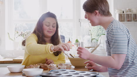 young downs syndrome couple decorating homemade cupcakes with marshmallows in kitchen at home